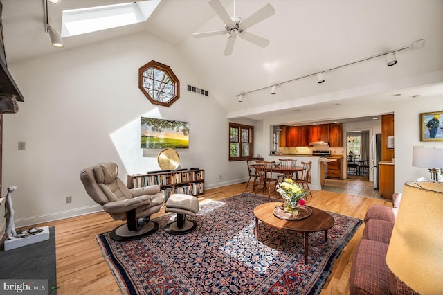living area with a skylight, a ceiling fan, rail lighting, and light wood-type flooring