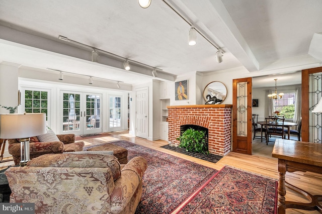 living room featuring wood finished floors, rail lighting, a fireplace, a notable chandelier, and french doors