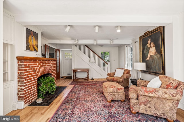 living room with wood finished floors, stairs, and a brick fireplace