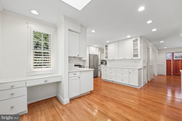 9373 Robnel Pl, Vienna, VA 22182 - kitchen featuring glass insert cabinets, a skylight, appliances with stainless steel finishes, light wood-style floors, and white cabinetry