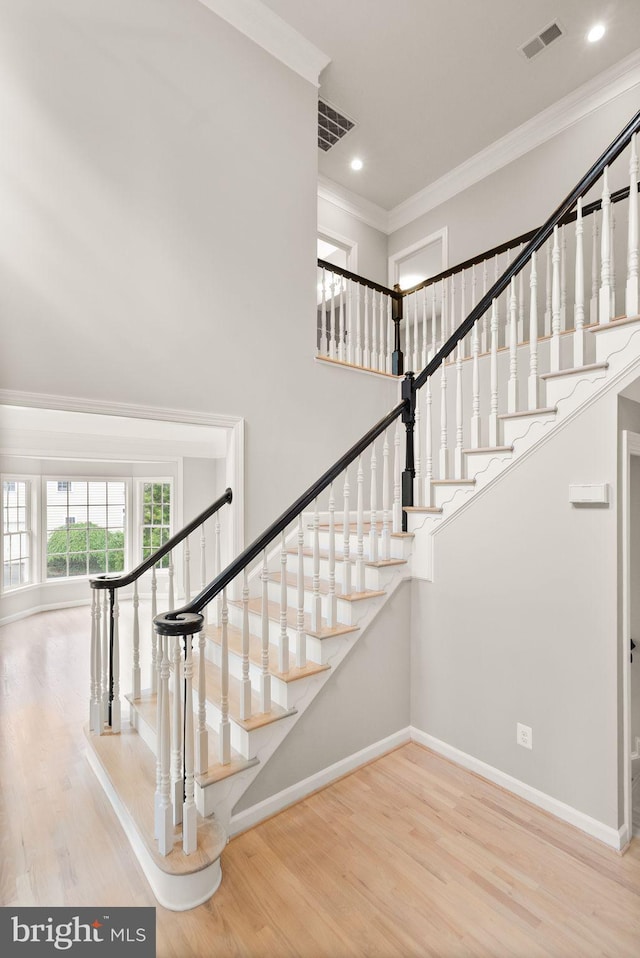 stairs with baseboards, ornamental molding, wood finished floors, a high ceiling, and recessed lighting