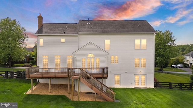 back of house at dusk with a wooden deck, a chimney, stairway, and roof with shingles