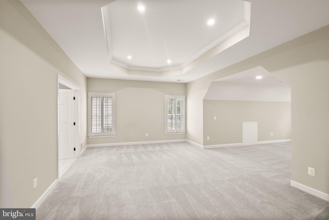 empty room featuring a raised ceiling, crown molding, light carpet, recessed lighting, and baseboards