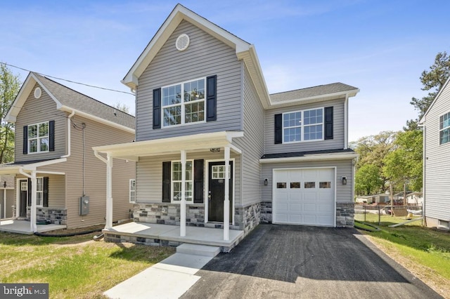 traditional-style home with covered porch, fence, driveway, stone siding, and an attached garage