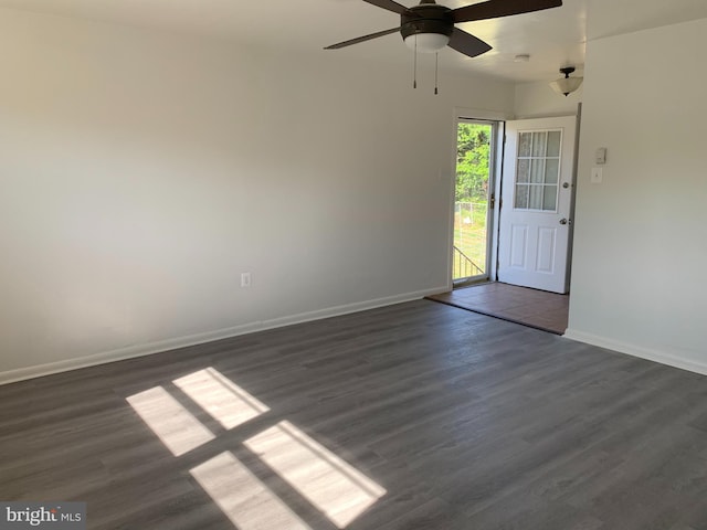 spare room featuring baseboards, ceiling fan, and dark wood finished floors