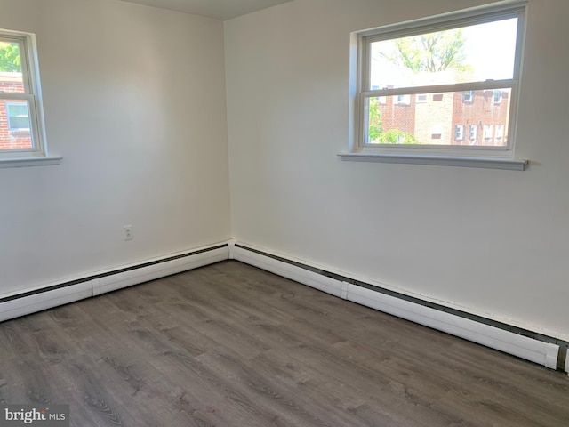 unfurnished room featuring a baseboard heating unit, wood finished floors, and a healthy amount of sunlight