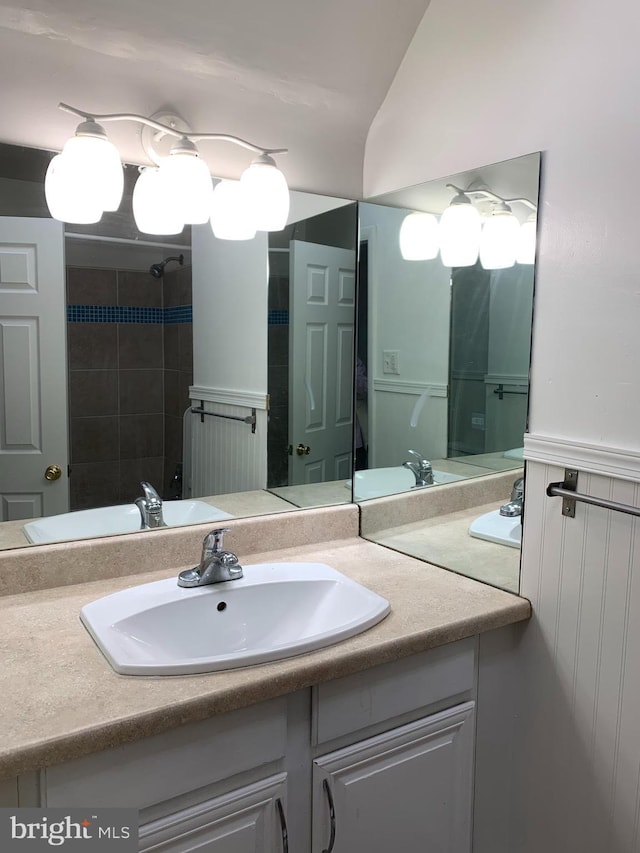 bathroom with lofted ceiling, vanity, and a wainscoted wall