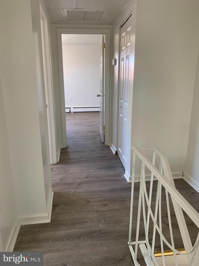 hall featuring wood finished floors, a paneled ceiling, a baseboard heating unit, and baseboards