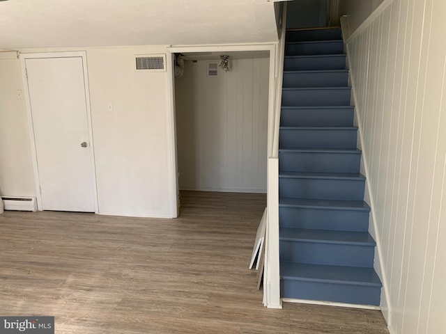 stairway featuring wood finished floors, visible vents, and baseboard heating