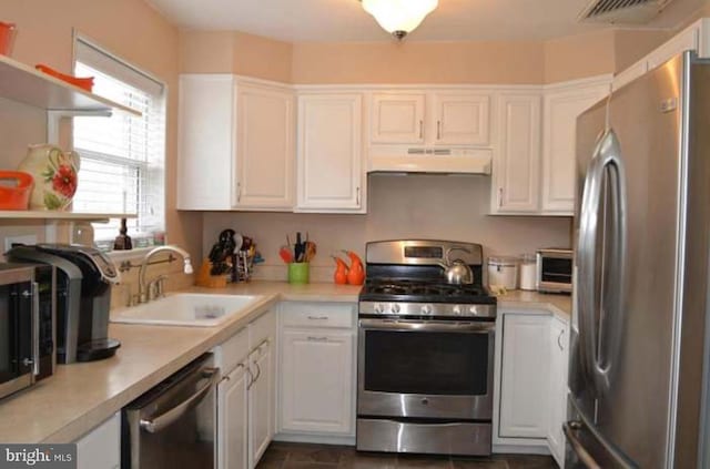 kitchen featuring under cabinet range hood, light countertops, appliances with stainless steel finishes, a sink, and white cabinetry