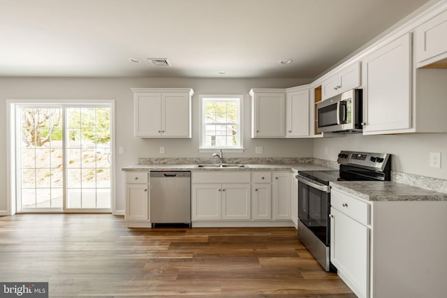 kitchen with appliances with stainless steel finishes, wood finished floors, white cabinetry, and a sink