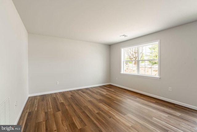 empty room featuring baseboards, visible vents, and wood finished floors