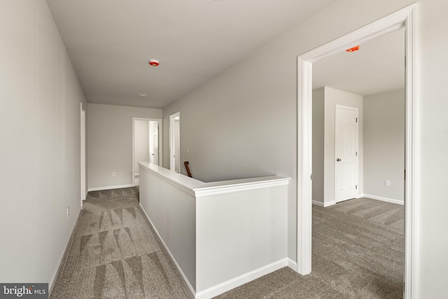 corridor featuring baseboards, an upstairs landing, and carpet
