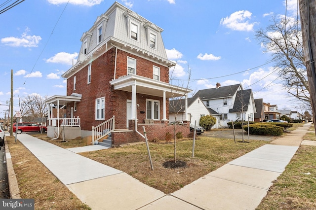 victorian home with a front lawn, a porch, and brick siding