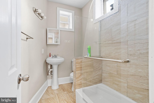 bathroom with toilet, a sink, a shower, and baseboards