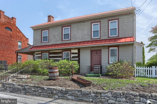 view of front of house with fence, a standing seam roof, a chimney, and metal roof