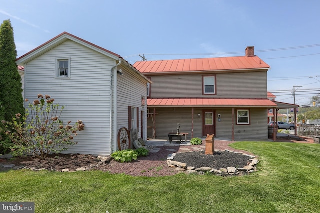 rear view of house featuring a standing seam roof, metal roof, a chimney, a lawn, and a patio