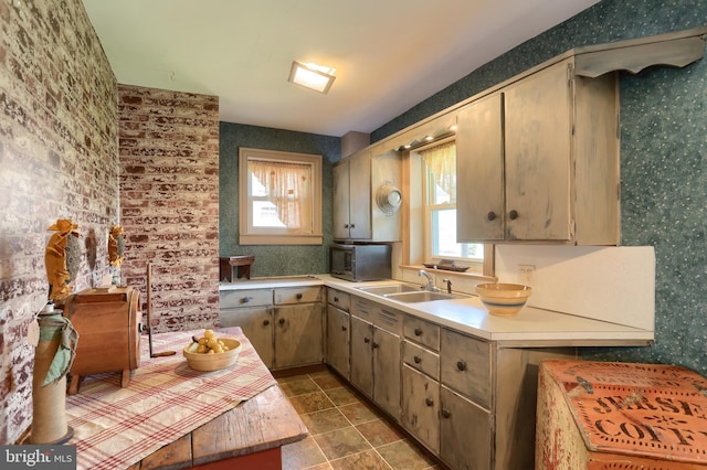 kitchen with a sink, light countertops, black microwave, and wallpapered walls