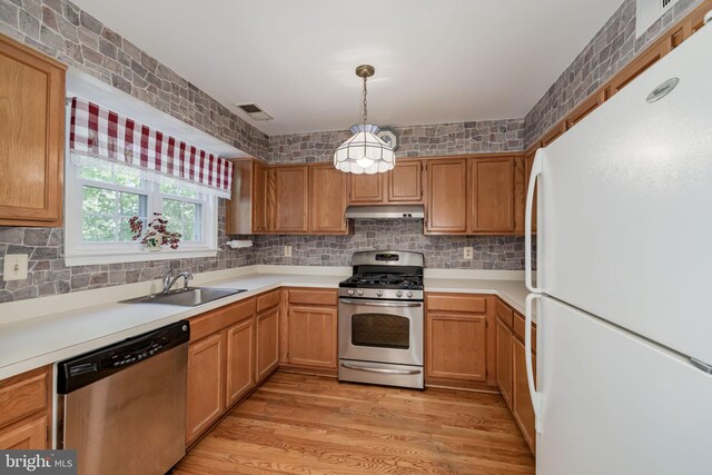kitchen featuring appliances with stainless steel finishes, a sink, decorative backsplash, under cabinet range hood, and visible vents