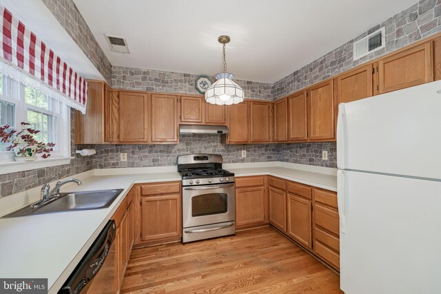 kitchen with a sink, stainless steel gas stove, freestanding refrigerator, under cabinet range hood, and dishwashing machine