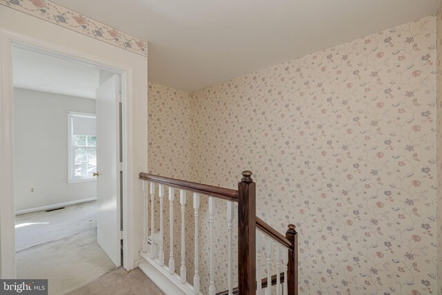 hall with carpet floors, visible vents, baseboards, and an upstairs landing