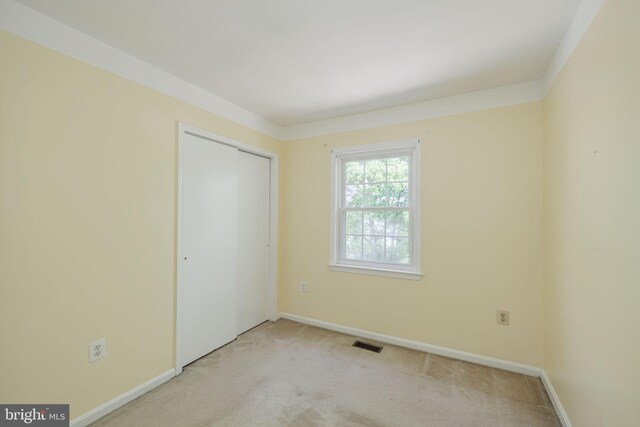 unfurnished bedroom featuring visible vents, baseboards, a closet, and light carpet