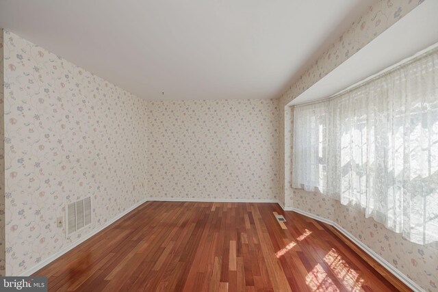 spare room with visible vents, wood finished floors, and wallpapered walls