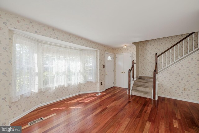 foyer entrance with wallpapered walls, visible vents, stairway, and hardwood / wood-style floors