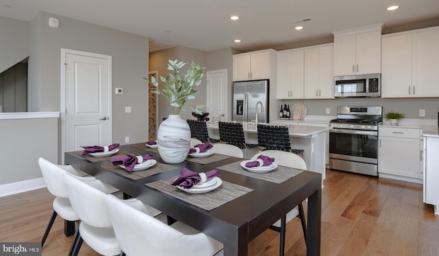 kitchen with white cabinetry, appliances with stainless steel finishes, light wood-style floors, light countertops, and an island with sink