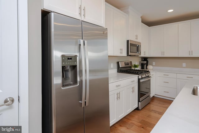 kitchen featuring recessed lighting, stainless steel appliances, light countertops, light wood finished floors, and white cabinetry