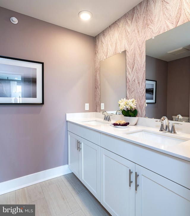 full bath with double vanity, baseboards, and a sink