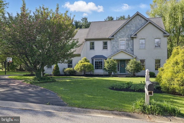 view of front of home featuring stucco siding, stone siding, and a front lawn