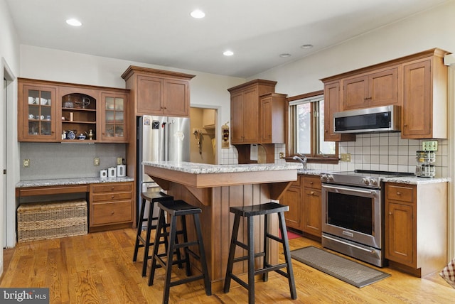 kitchen featuring glass insert cabinets, light wood-style floors, a kitchen bar, tasteful backsplash, and stainless steel appliances