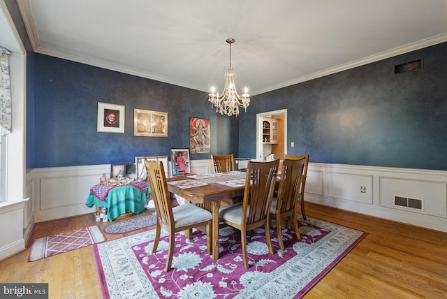 dining space featuring a wainscoted wall, a notable chandelier, wood finished floors, and visible vents