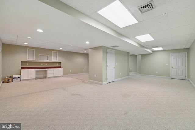 finished below grade area with visible vents, baseboards, light carpet, and a paneled ceiling