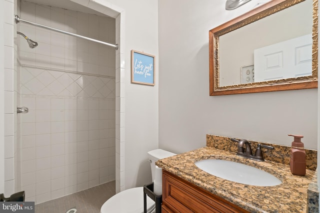 bathroom featuring vanity, a tile shower, and toilet