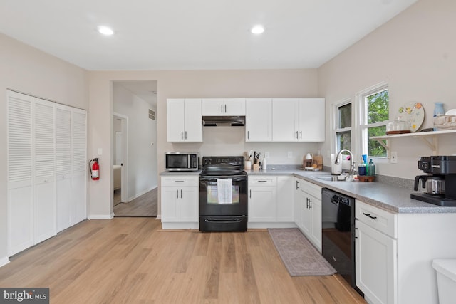kitchen with white cabinetry, under cabinet range hood, a sink, light wood finished floors, and black appliances
