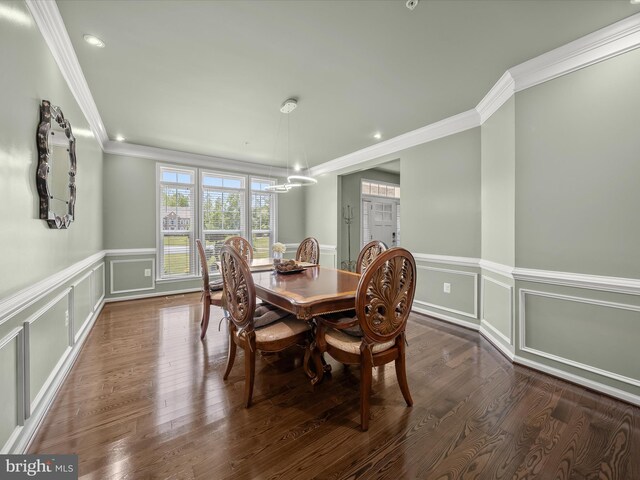 dining room with crown molding, a chandelier, a decorative wall, a wainscoted wall, and dark wood-type flooring