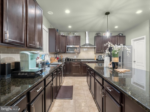 kitchen featuring wall chimney range hood, stainless steel appliances, a sink, decorative backsplash, and dark brown cabinetry