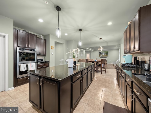 kitchen with stainless steel double oven, dark brown cabinetry, a kitchen island, light tile patterned flooring, and pendant lighting