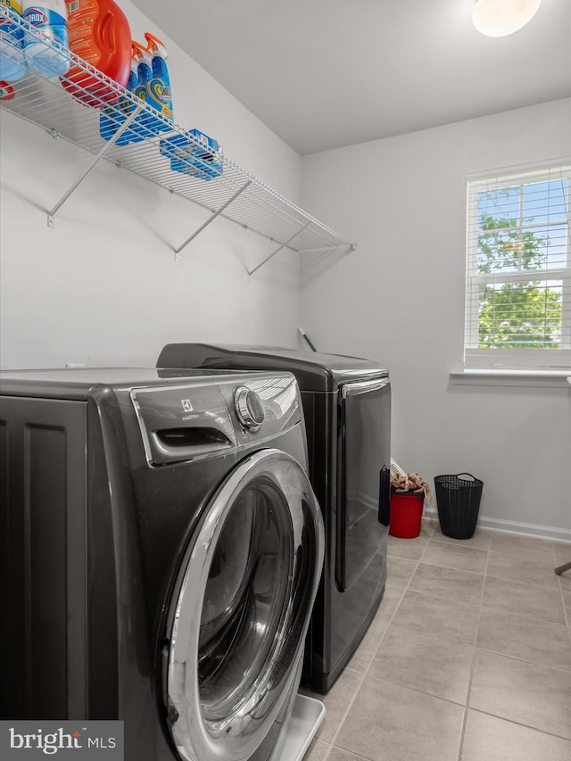 clothes washing area with separate washer and dryer, light tile patterned floors, and baseboards
