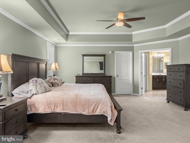 bedroom featuring a raised ceiling, crown molding, light carpet, ensuite bathroom, and baseboards