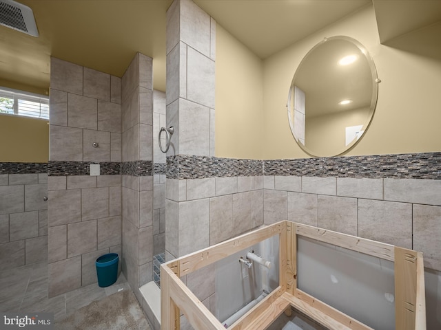 full bath featuring tiled shower and tile walls