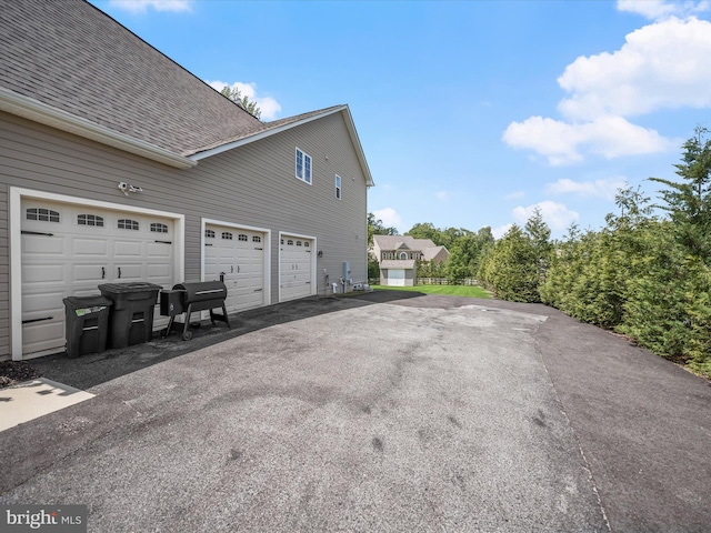 view of side of property with asphalt driveway, roof with shingles, and an attached garage