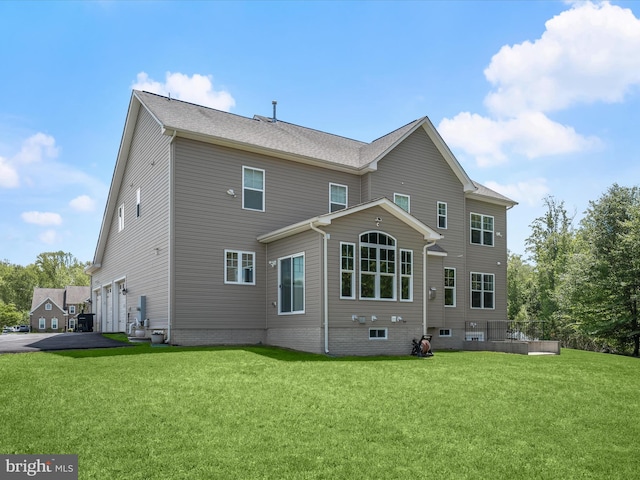 rear view of house with an attached garage, a lawn, and driveway