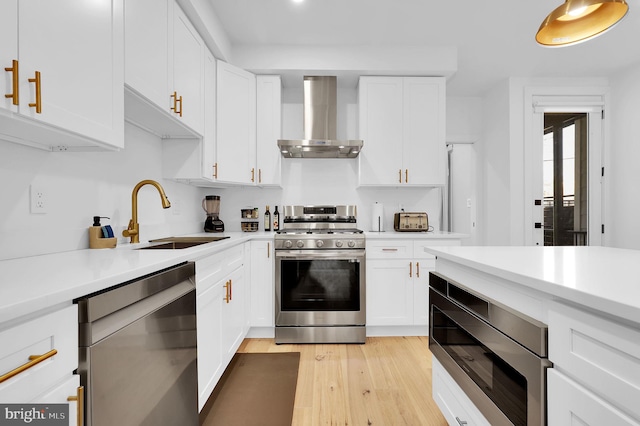 kitchen with light countertops, appliances with stainless steel finishes, a sink, and wall chimney exhaust hood