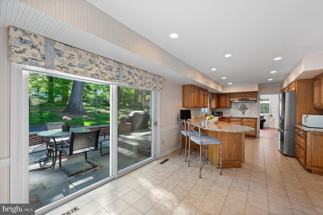 kitchen with a peninsula, freestanding refrigerator, brown cabinets, and white microwave