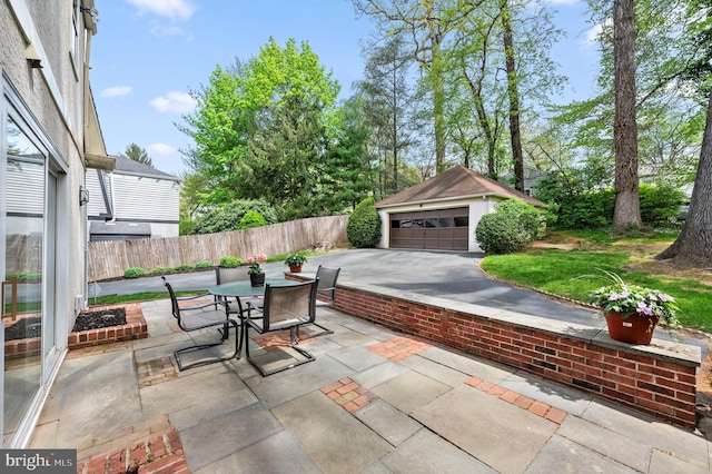 view of patio featuring outdoor dining area, a garage, fence, and an outbuilding