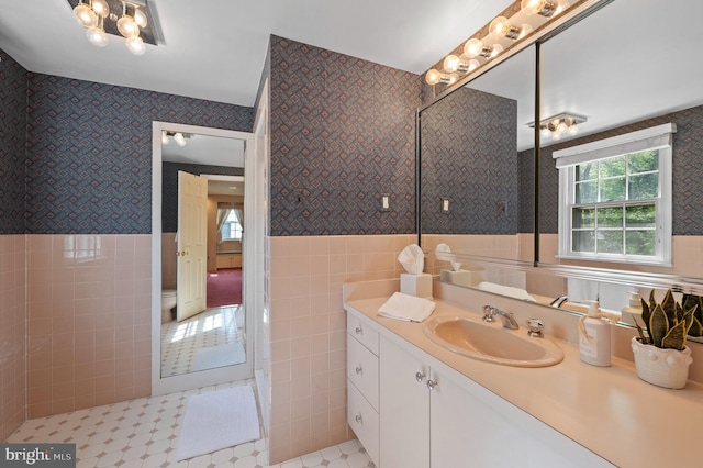 bathroom with wallpapered walls, tile walls, wainscoting, and vanity