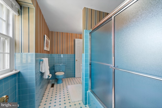 bathroom with a healthy amount of sunlight, tile walls, tile patterned floors, toilet, and a shower with door